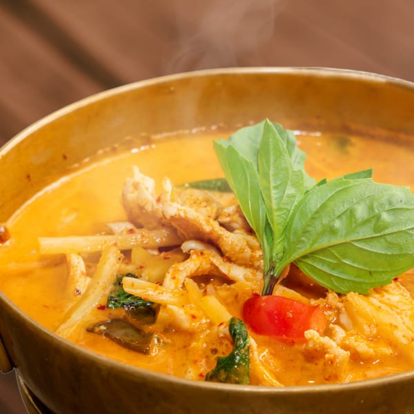 Steaming Sampannee Thai red curry with chicken, bamboo shoots, basil, and red pepper in a golden pot.