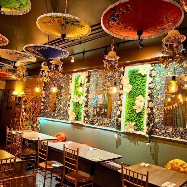 Sampannee Thai restaurant interior with colorful umbrellas, floral wallpaper, and green plant accents.