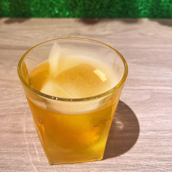 A glass of golden iced tea with a large ice cube on a wooden table.