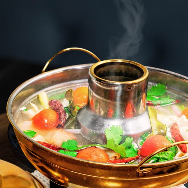 Steaming Thai hot pot with tomatoes, chili, and herbs in a golden pot.