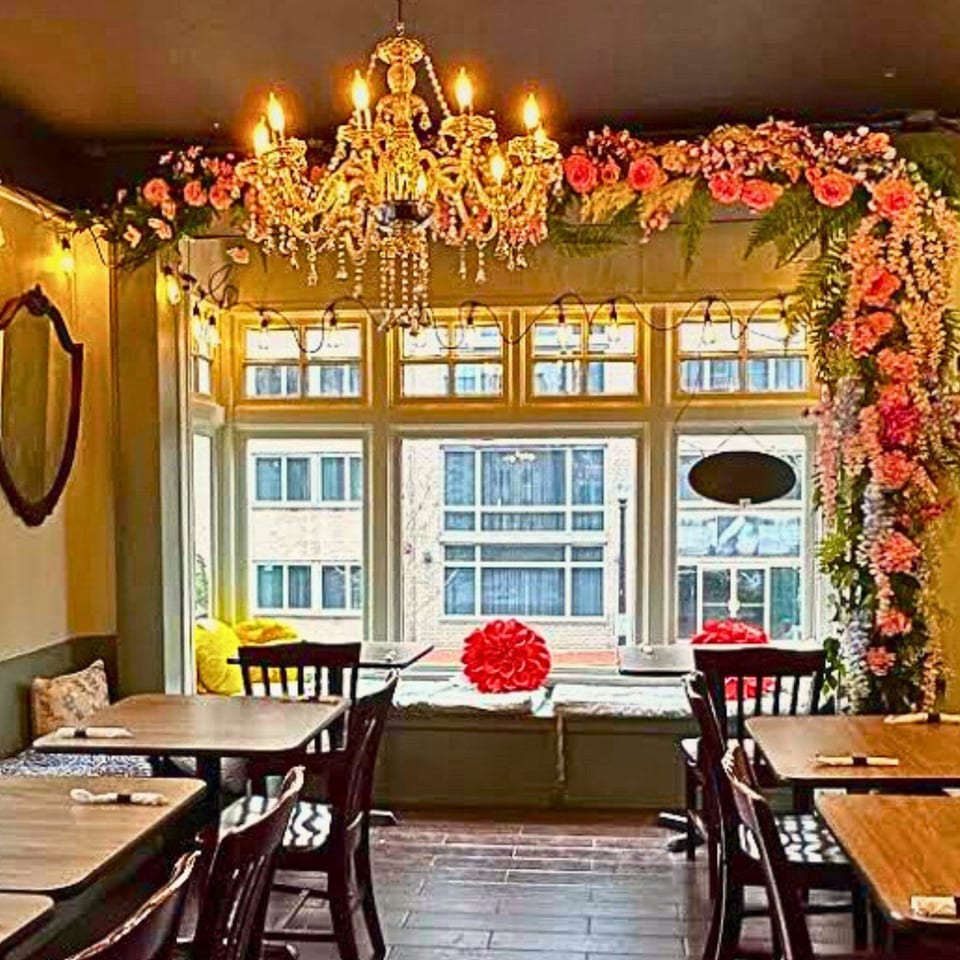 Sampannee Thai restaurant interior with tables, chairs, a chandelier, and floral decorations around a large window.
