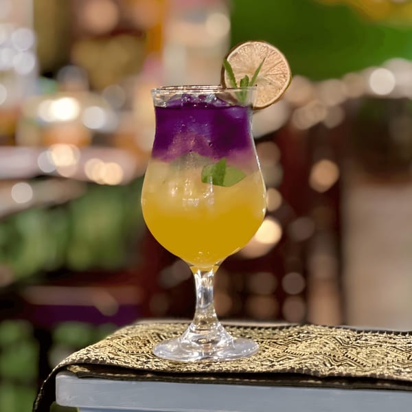 A vibrant two-toned drink, purple over yellow, garnished with lime and mint, on a patterned mat.