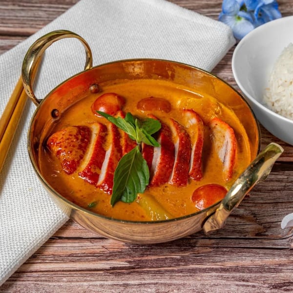 Sampannee Thai red curry with sliced duck, cherry tomatoes, and basil in a brass pot.