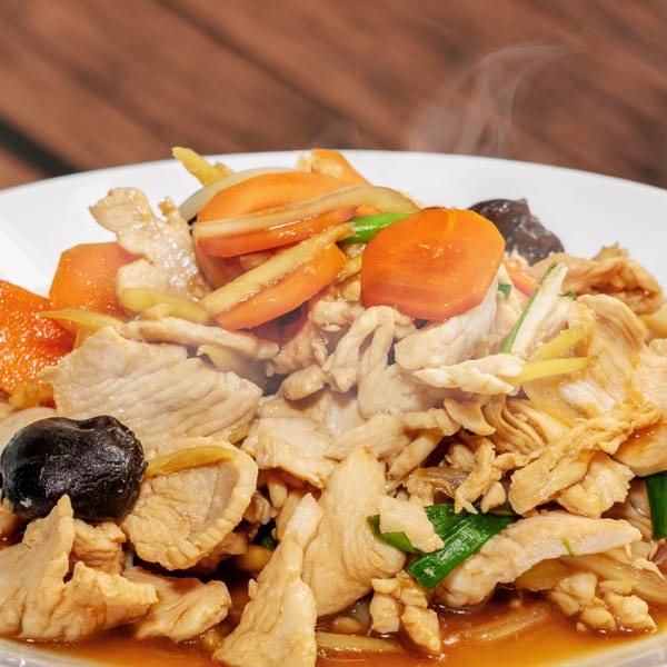 Steaming Thai chicken stir-fry with carrots, mushrooms, and green onions on a white plate.